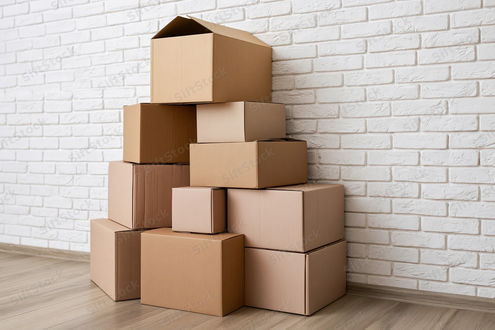 Stack of cardboard moving boxes piled against a white brick wall in a room