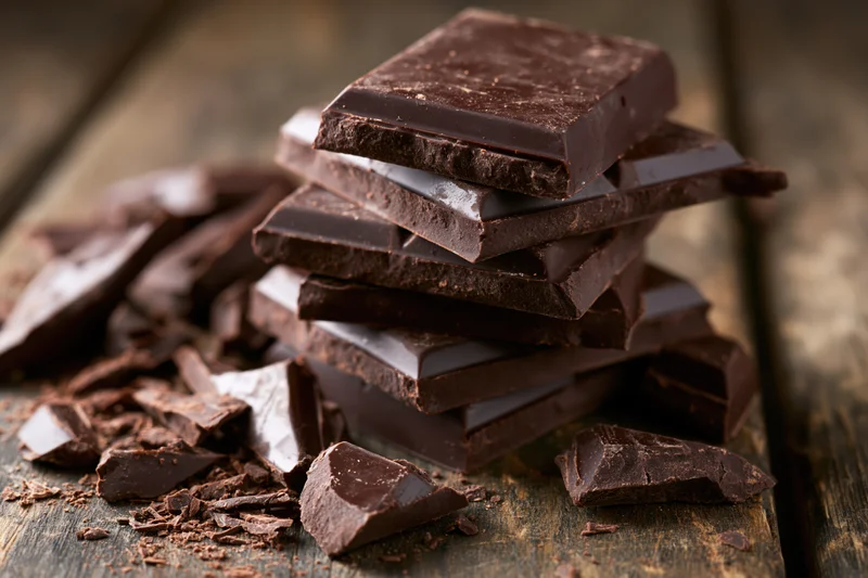 Dark chocolate squares stacked unevenly on worn wooden surface