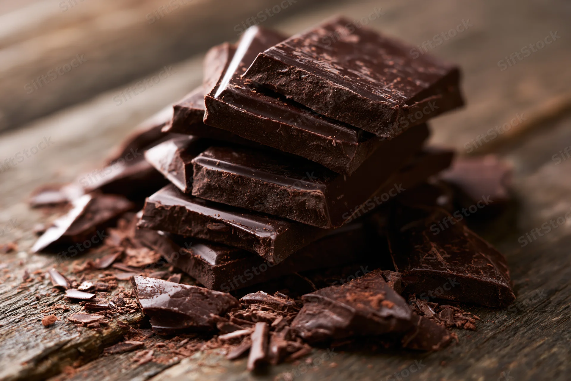 Dark chocolate pieces stacked unevenly on worn wooden surface
