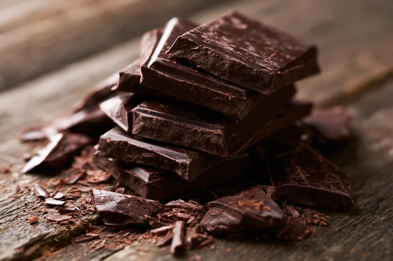 Dark chocolate pieces stacked unevenly on worn wooden surface