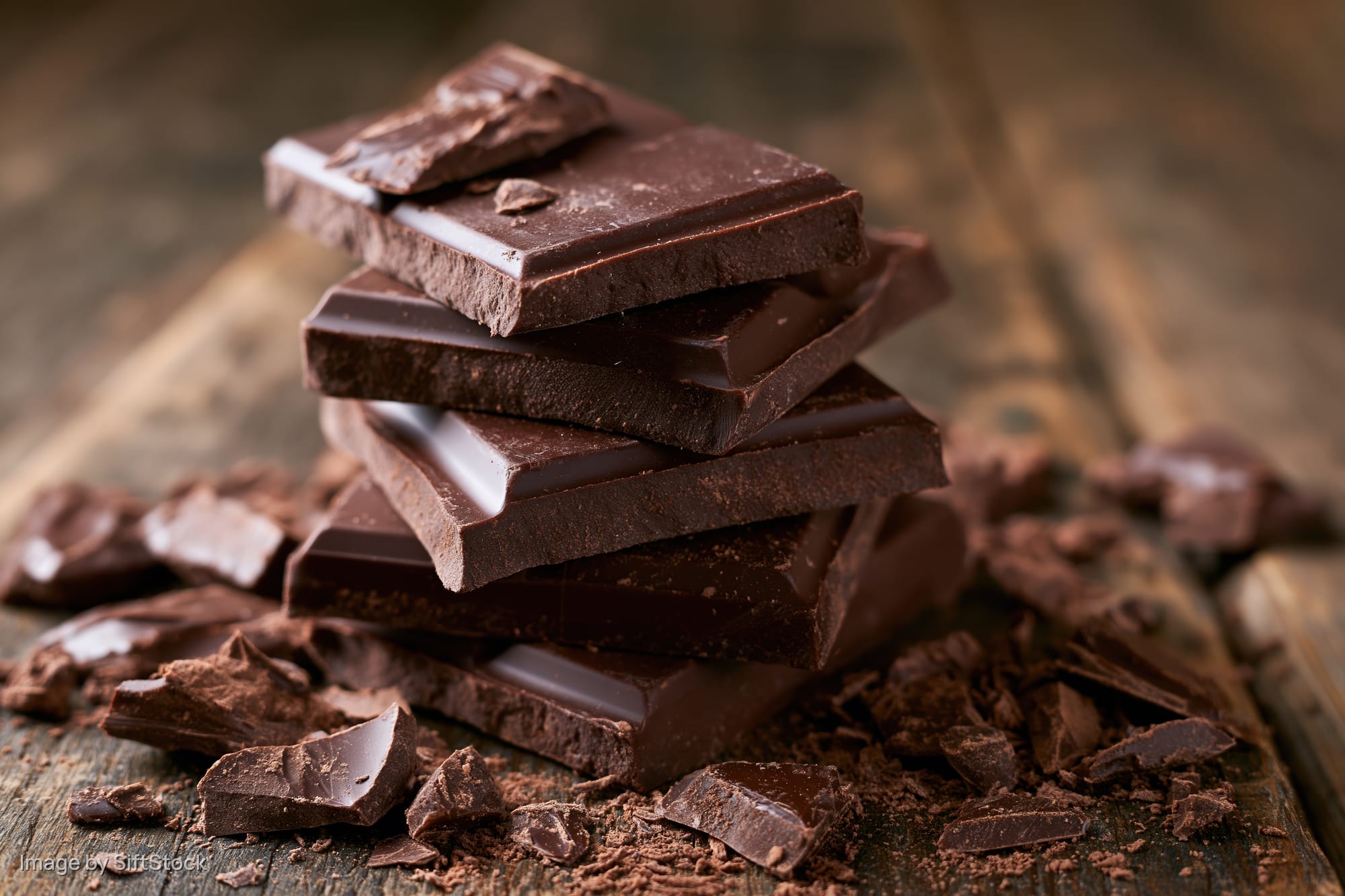 Stack of dark chocolate squares piled unevenly on a worn wood