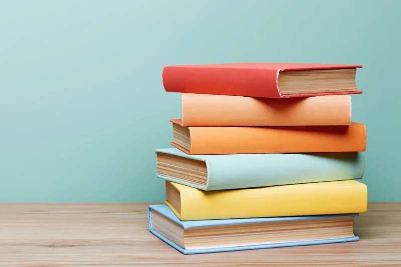 Stack of six colorful hardcover books arranged on a light wood desk