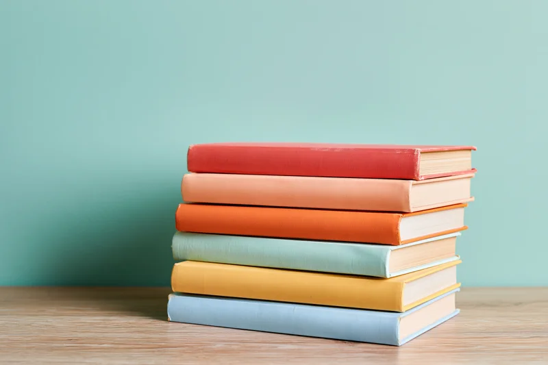 Stack of six colorful hardcover books on a light wood desk