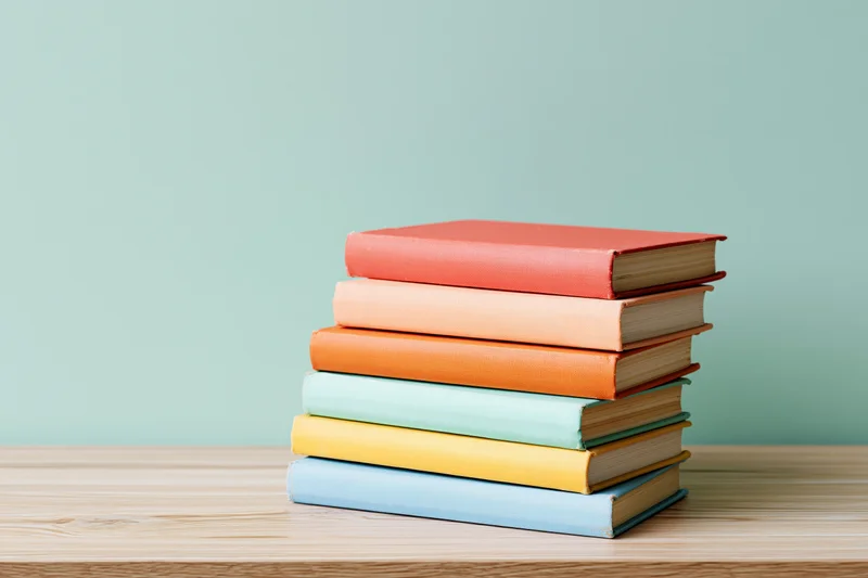 Stack of six colorful hardcover books on a light wood desk