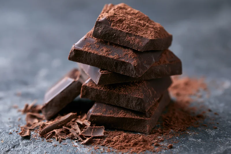 Stacked broken dark chocolate chunks dusted with cocoa powder on a dark surface