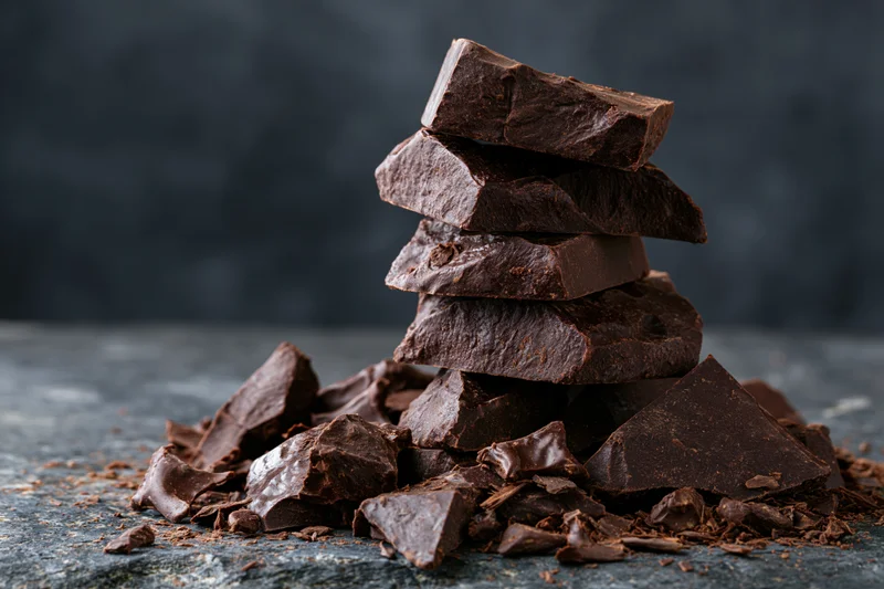 Broken dark chocolate chunks stacked and scattered on a rough slate surface
