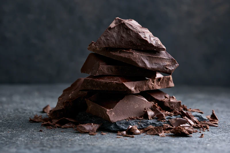 Broken dark chocolate chunks stacked in a pile on a rough slate surface