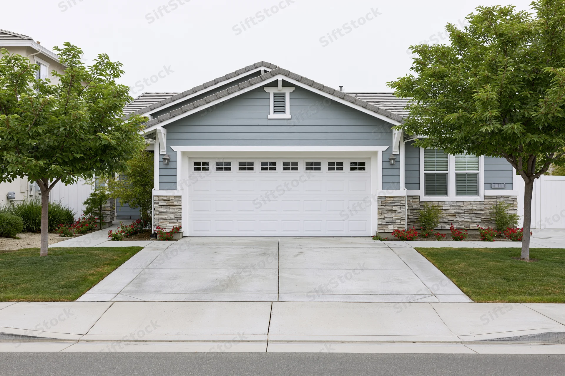 Suburban single-story house with white two-car garage and concrete driveway fronted by lawn and trees