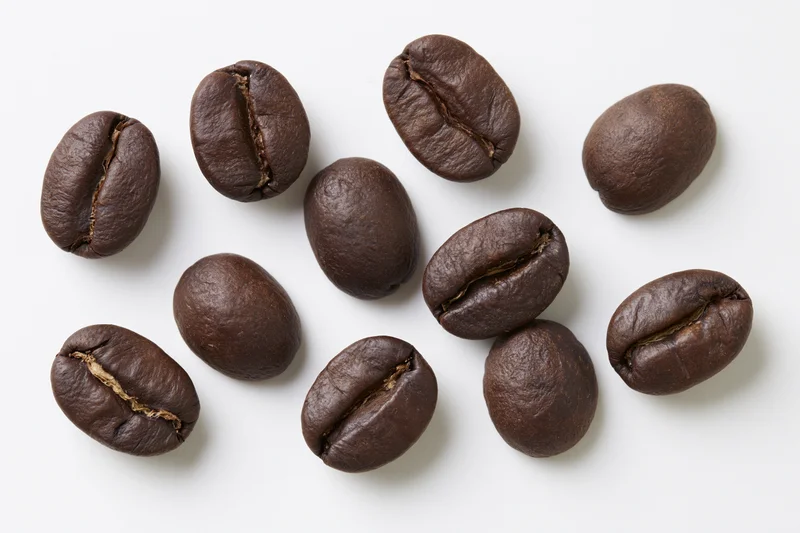 Roasted coffee beans scattered on a white surface in a top-down view