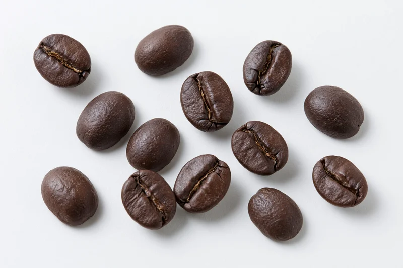 Roasted coffee beans scattered on a white background in a top-down closeup view