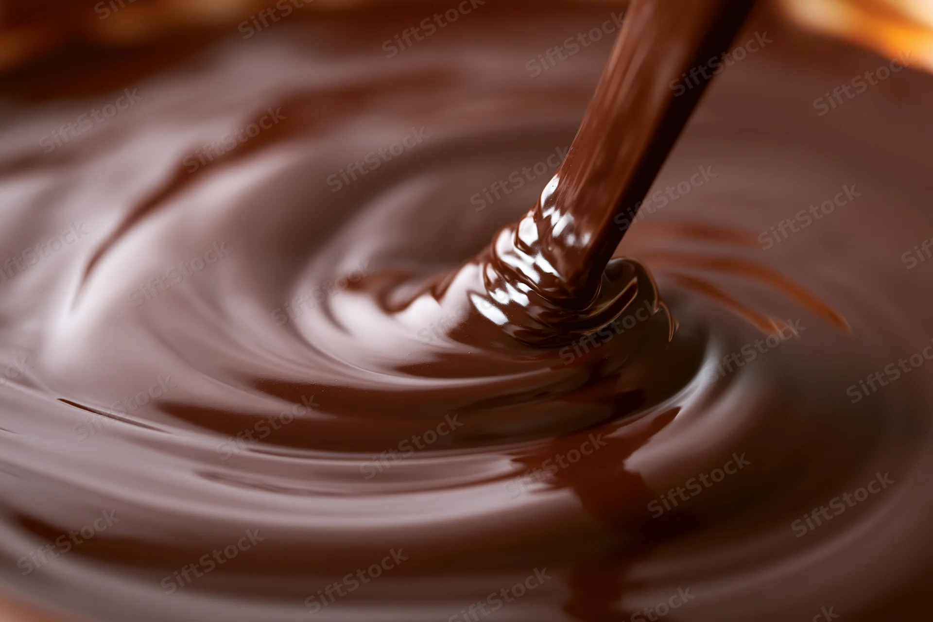 Thick stream of melted dark chocolate pouring into a bowl, creating ripples on the glossy surface