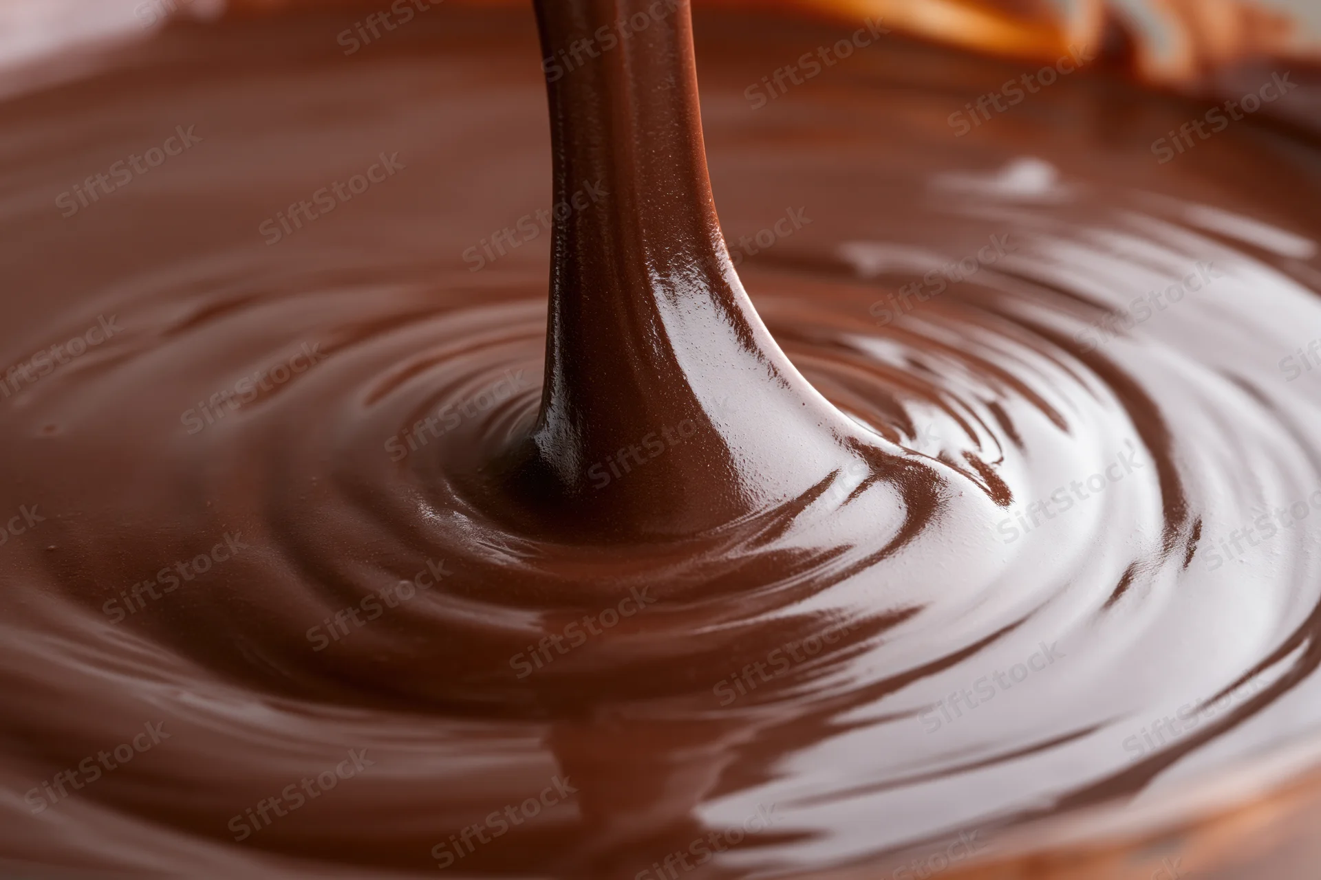 Thick stream of melted dark chocolate pouring into a bowl creating ripples and swirls