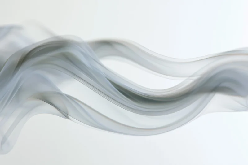 Thin wisp of white smoke curling and rising in soft undulating waves against a light background