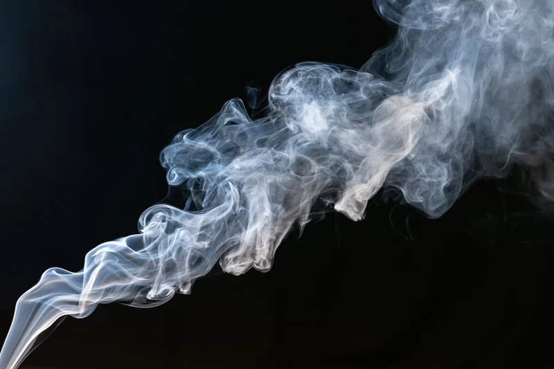 White smoke curling and dispersing midair against black background