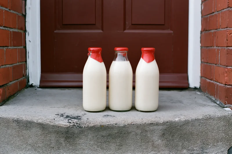 Three glass milk bottles with red foil caps on a concrete doorstep in front of a red door