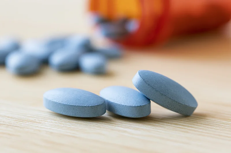 Pale blue oval tablets resting on a light wood surface with an orange bottle in the background