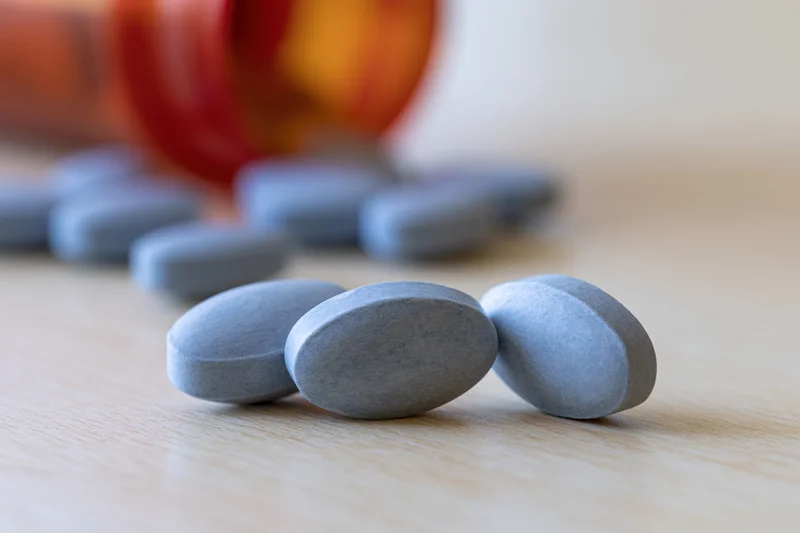 Pale blue oval tablets resting on light wood surface with blurred amber bottle in background