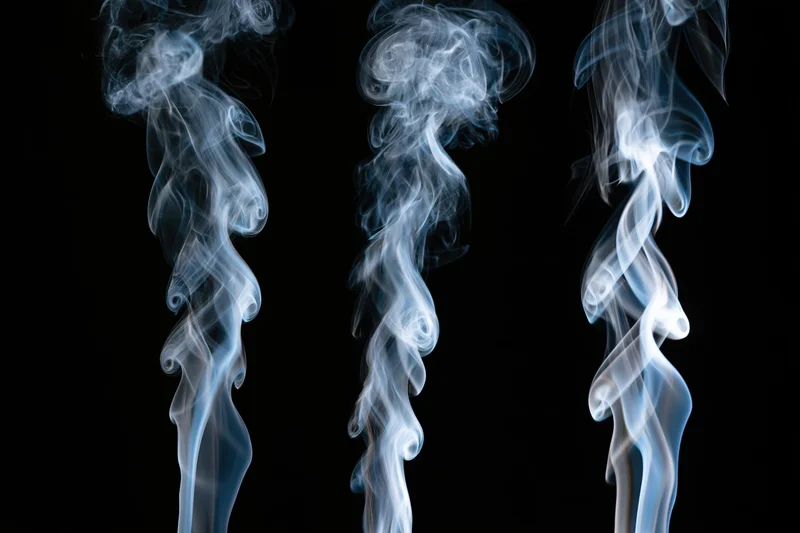 Three columns of rising white and pale blue smoke against a black background