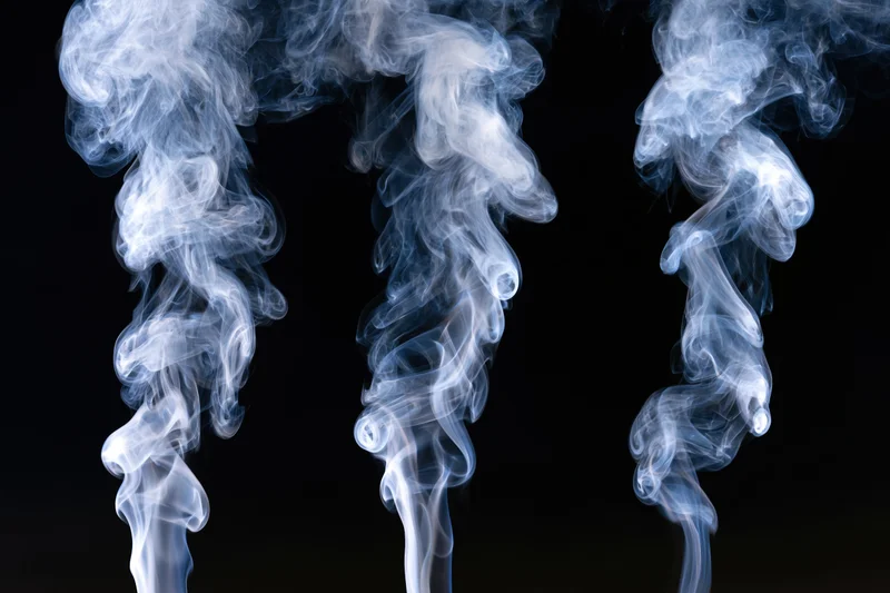 Three columns of white and pale blue smoke rising against a black background