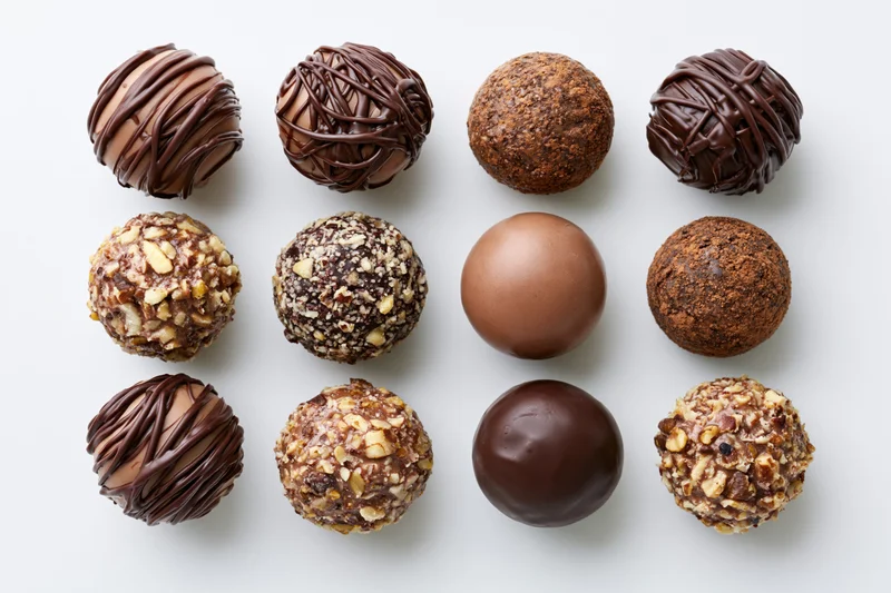 Twelve assorted chocolate truffles and pralines arranged in a grid on white background