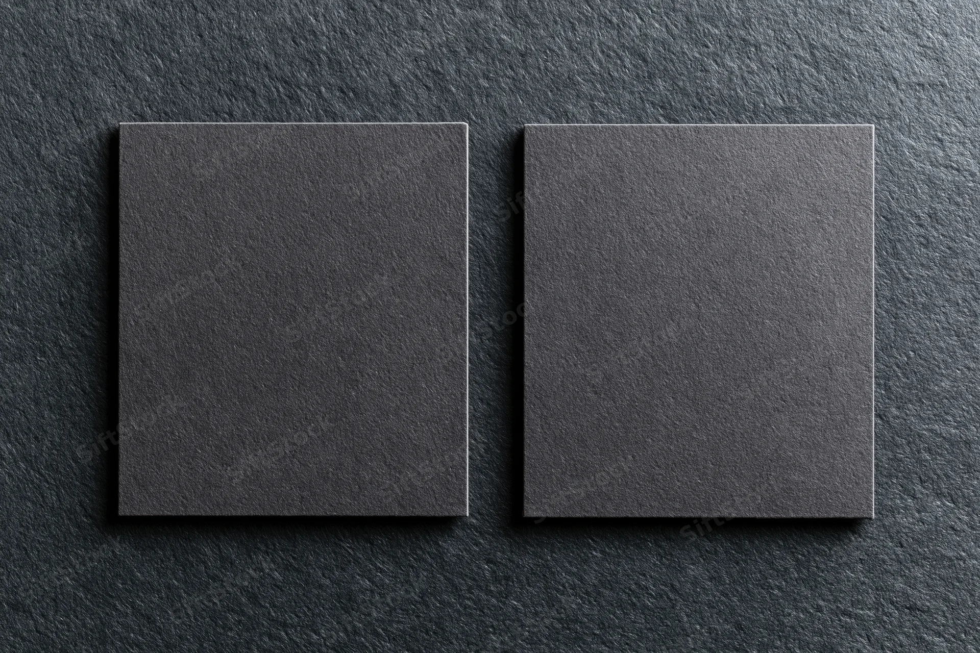 Two blank dark grey business cards lying flat side by side on a textured dark surface