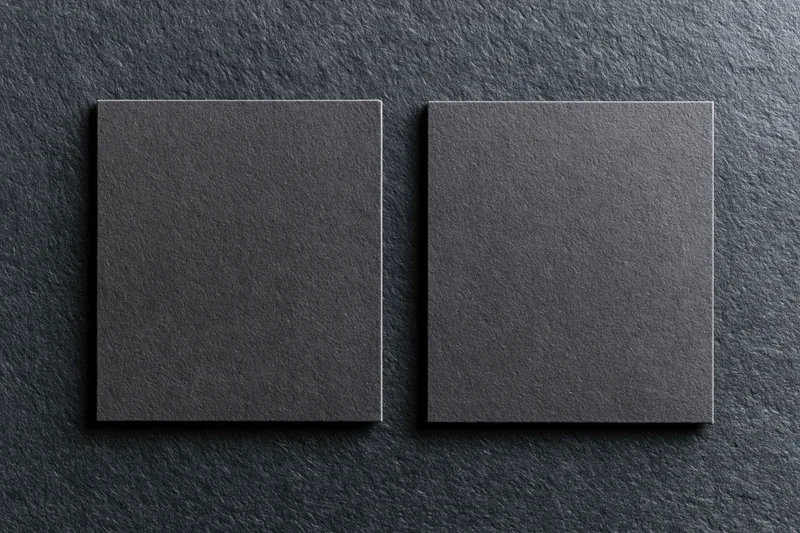 Two blank dark grey business cards lying flat side by side on a textured dark surface