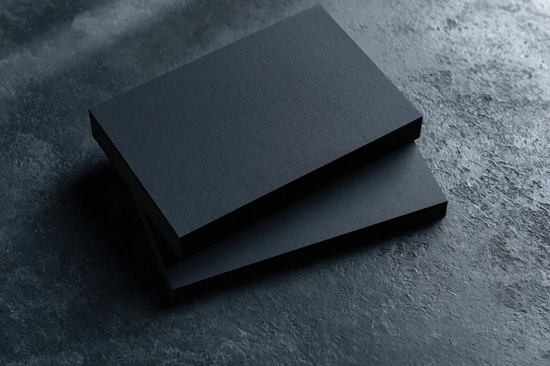 Two blank matte black business cards stacked slightly offset on a dark textured surface