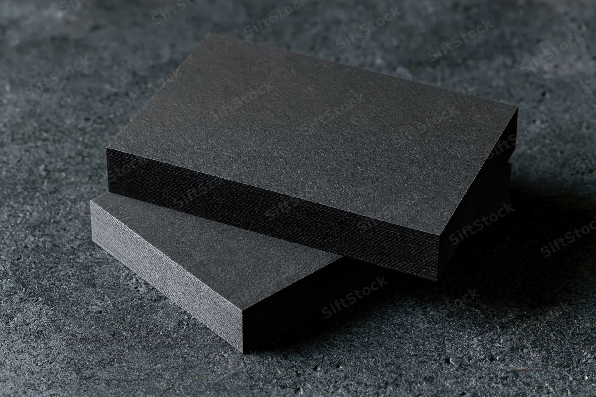 Two blank matte black business cards stacked slightly offset on a dark textured surface