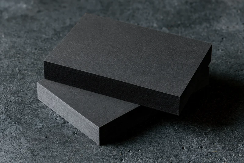 Two blank matte black business cards stacked slightly offset on a dark textured surface