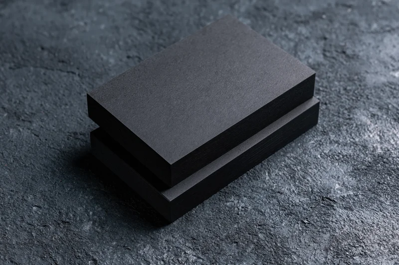 Two blank matte black business cards stacked slightly offset on a dark textured surface