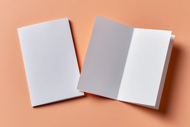 Two blank white bifold brochures lying flat on a peach-orange surface