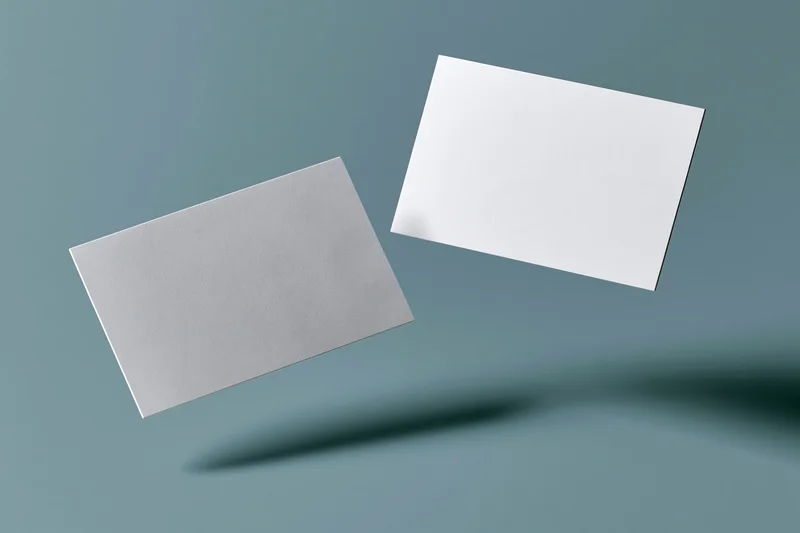 Two blank white business cards floating at slight angles against a blue-gray gradient background