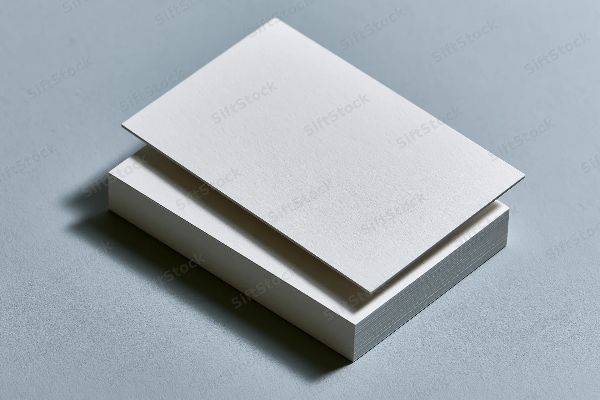 Stack of blank white business cards on gray surface with one card slightly offset for design mockup