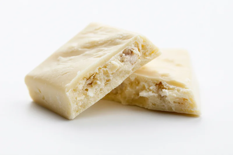 Two broken white chocolate pieces stacked at an angle showing interior texture