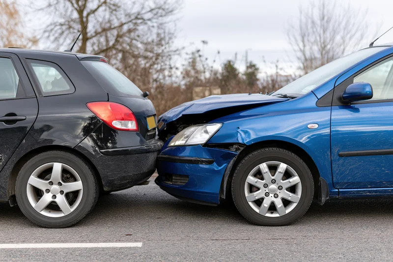 Two hatchback cars collided rear-end on asphalt road showing damage to bumpers and fenders
