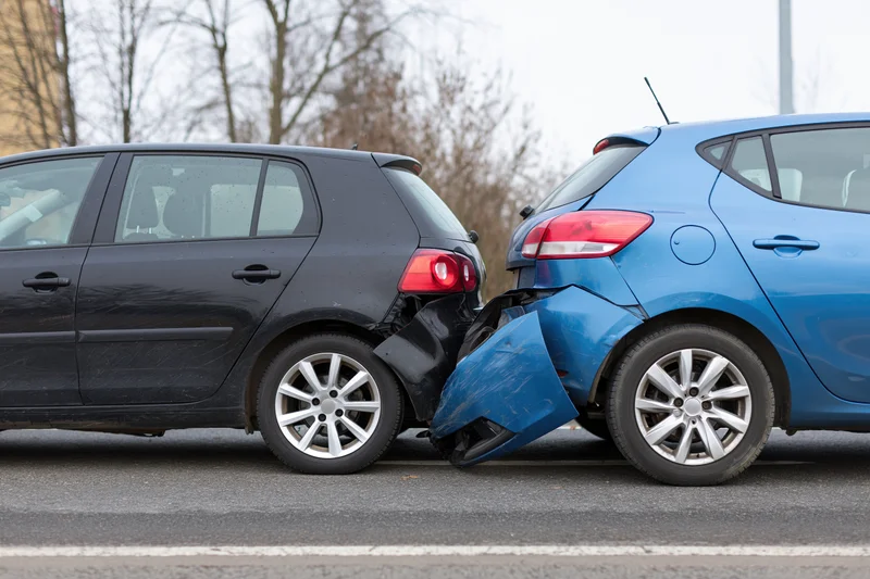 Two hatchbacks involved in a rear-end collision on a road with visible bumper damage