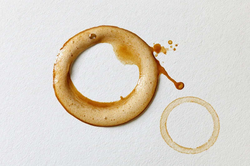 Coffee ring stains on white paper surface with foam and drip marks