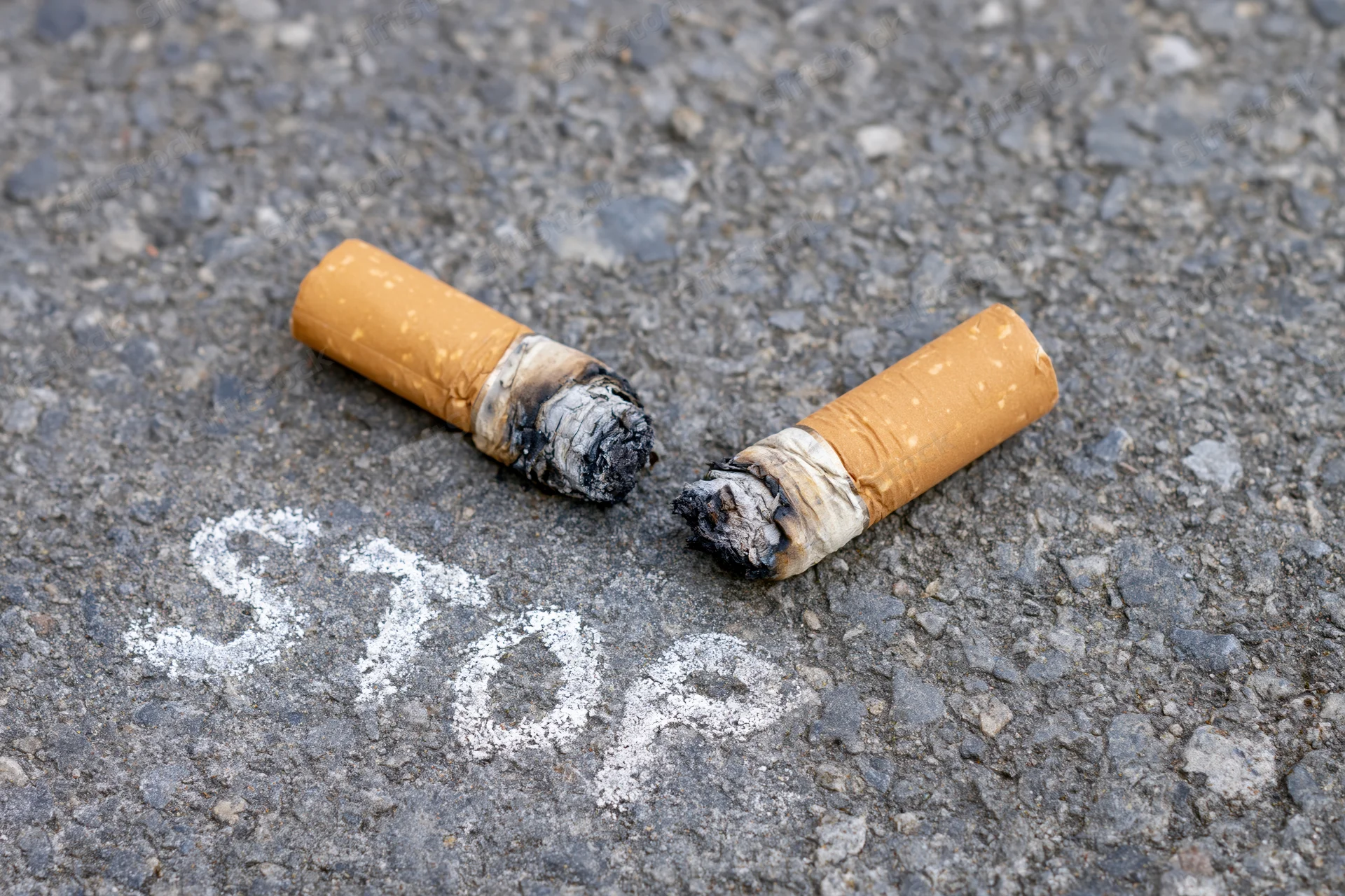 Two crushed cigarette butts on asphalt with stop written in chalk