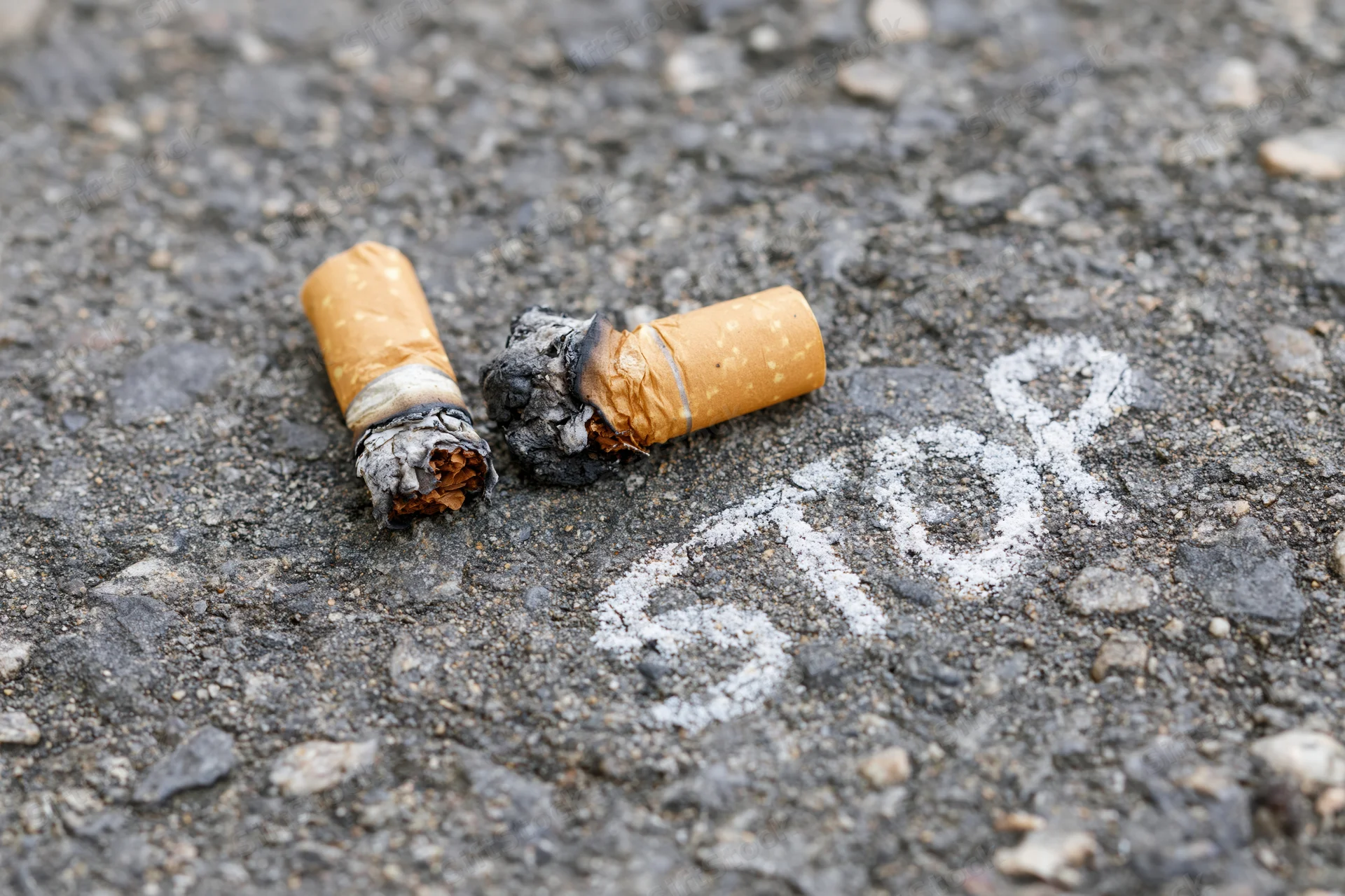 Two crushed cigarette butts with burnt ends lying on asphalt pavement near chalk-written stop sign