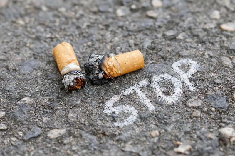 Two crushed cigarette butts with burnt ends lying on asphalt pavement near chalk-written stop sign