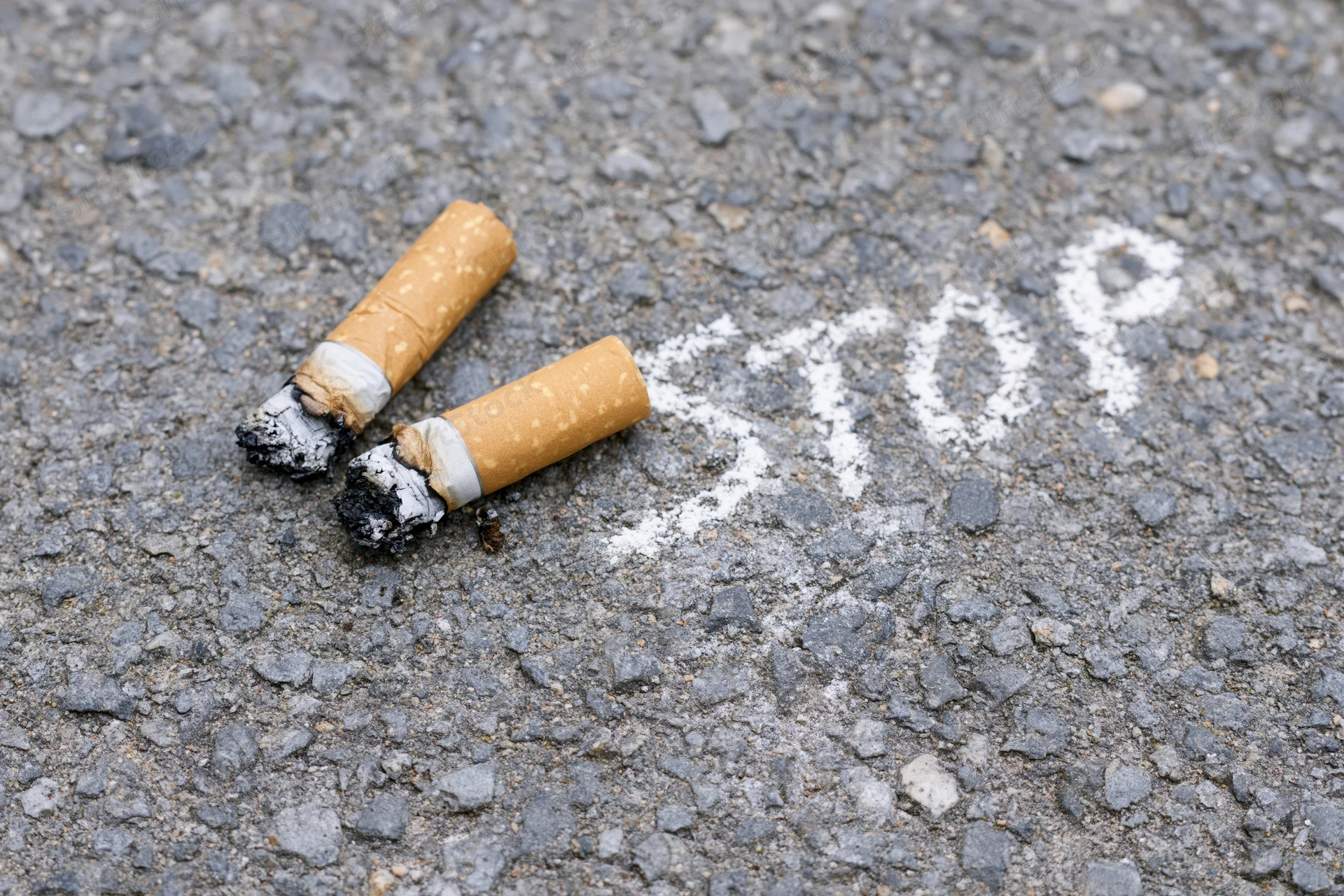 Crushed cigarette butts with stop written in ash on pavement