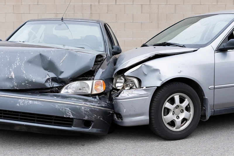Two damaged cars collided front-end on asphalt near a concrete wall