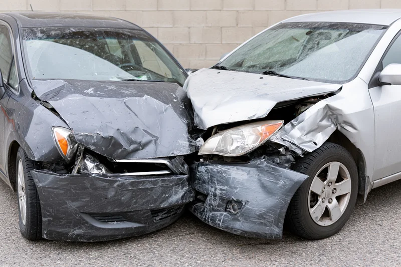 Two damaged cars collided front-end on asphalt near concrete wall