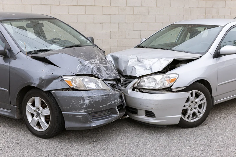 Two damaged cars collided front-end in a parking lot against a cinderblock wall