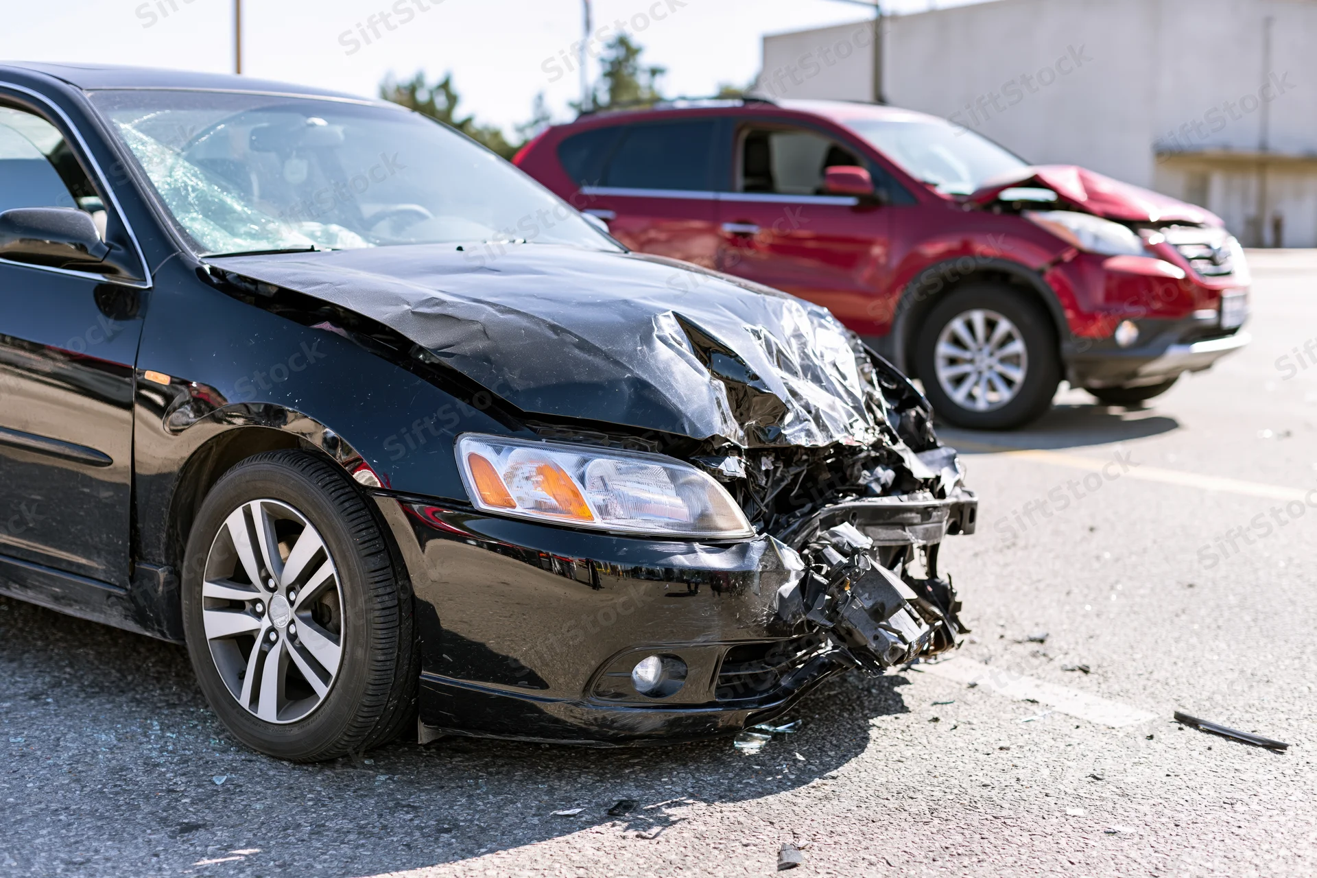 Black sedan with crumpled front end and broken bumper after collision in parking lot