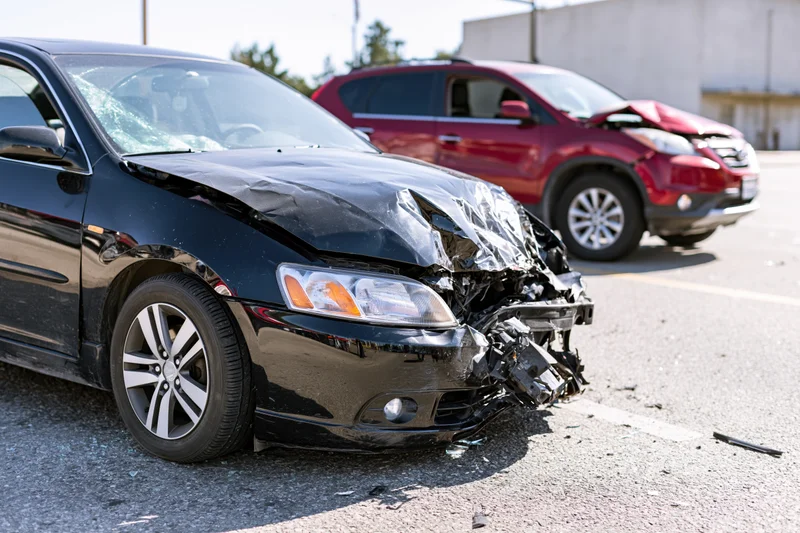 Black sedan with crumpled front end and broken bumper after collision in parking lot