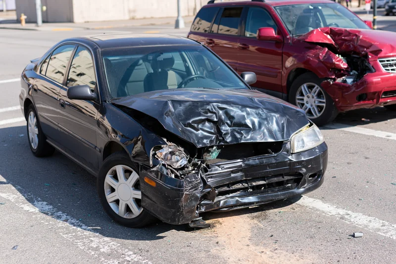 Two damaged cars parked in a lot after a collision, front ends crumpled and broken