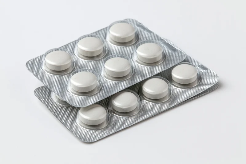 Two silver aluminum blister packs of round white pills stacked on white background