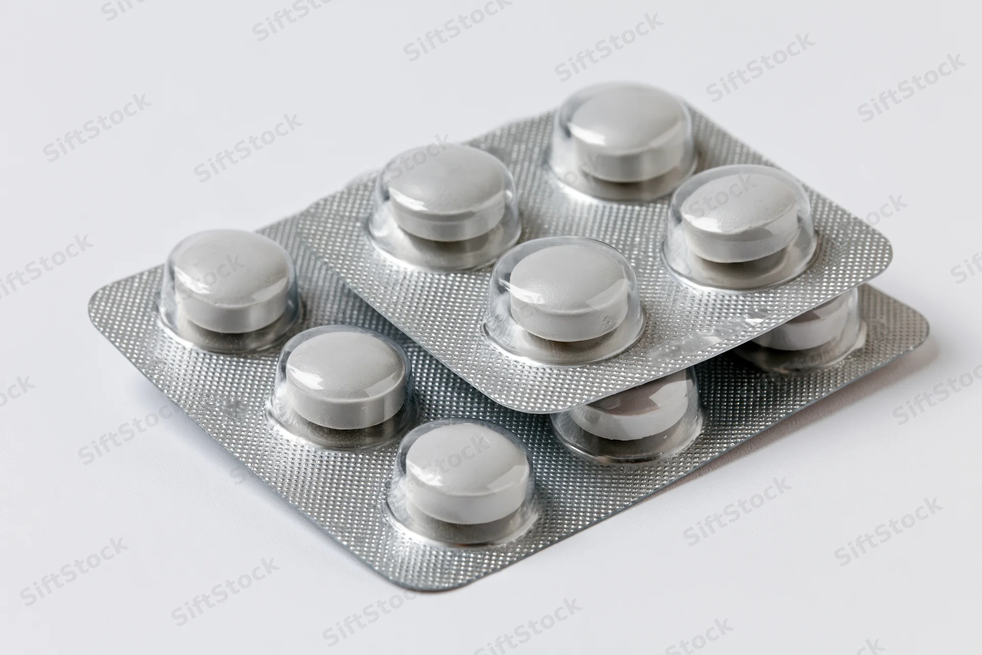 Two silver aluminum blister packs of round white pills stacked on white surface