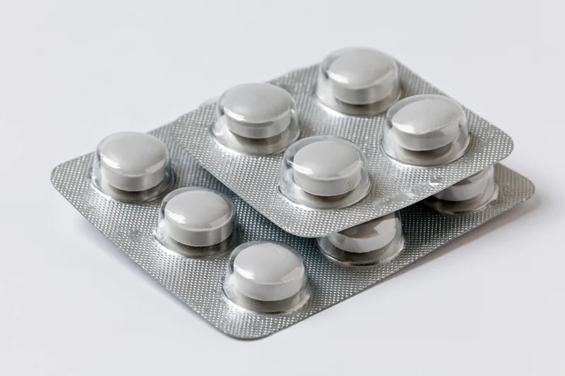 Two silver aluminum blister packs of round white pills stacked on white surface